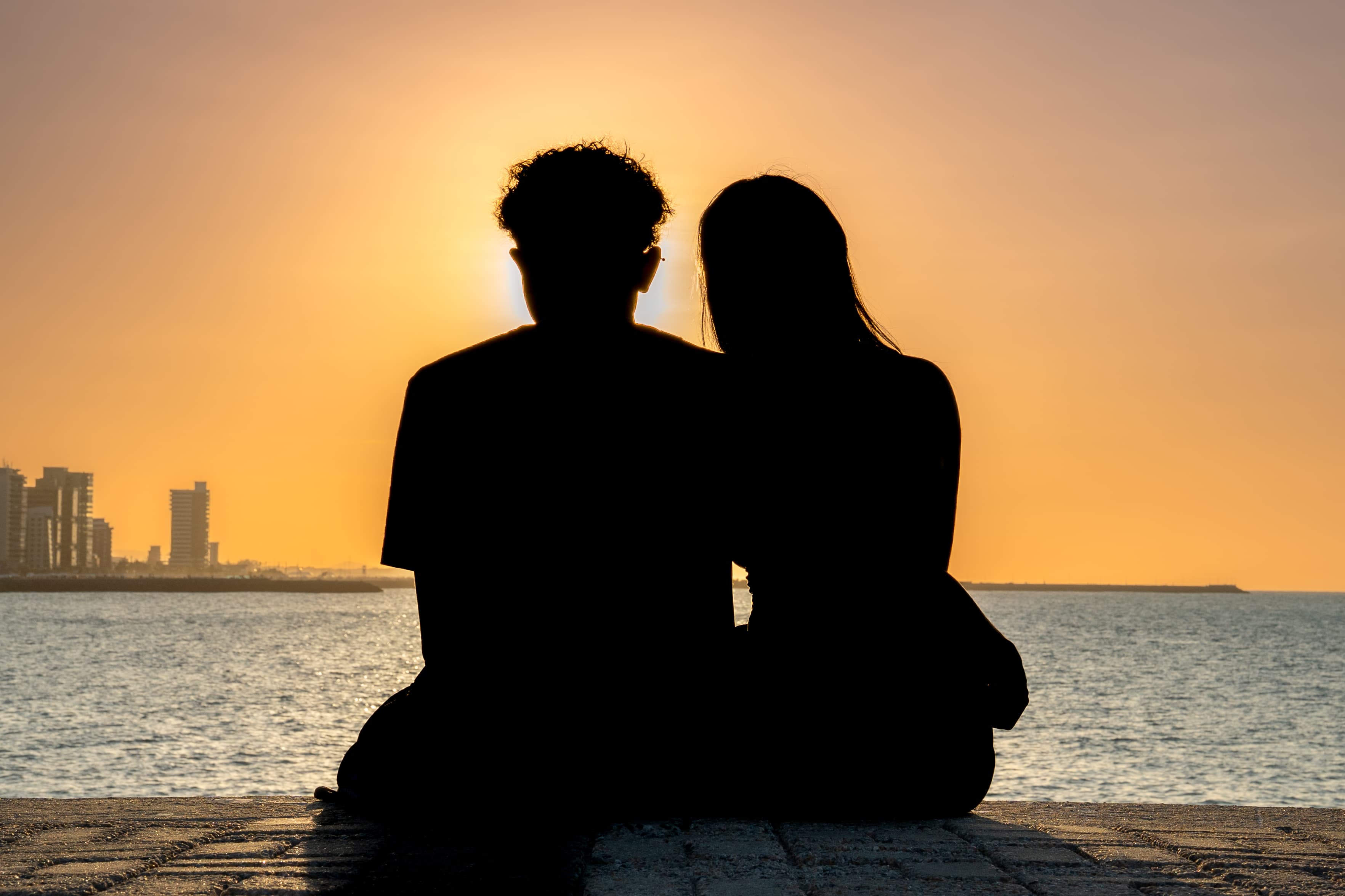 casal sentado na praia durante o pôr do sol